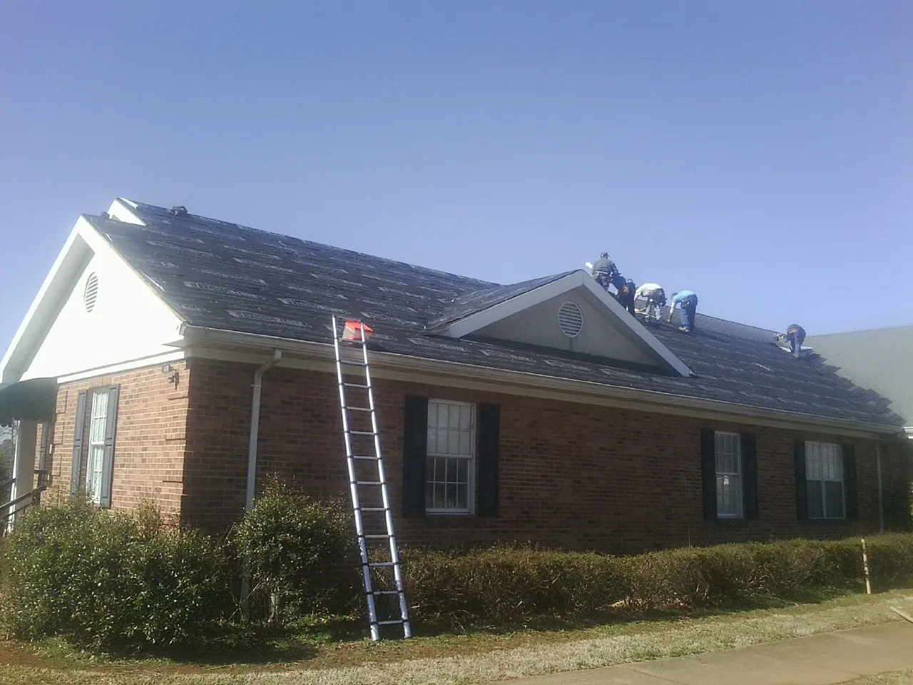 Crew tearing shingles off a brick ranch roof with a ladder set — Metal Roof Repair work by our crew in Somerville