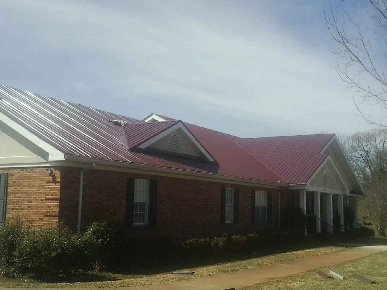 Red metal roof with gabled entries on a long brick building, from a Hail Damage Roof Repair job in Somerville