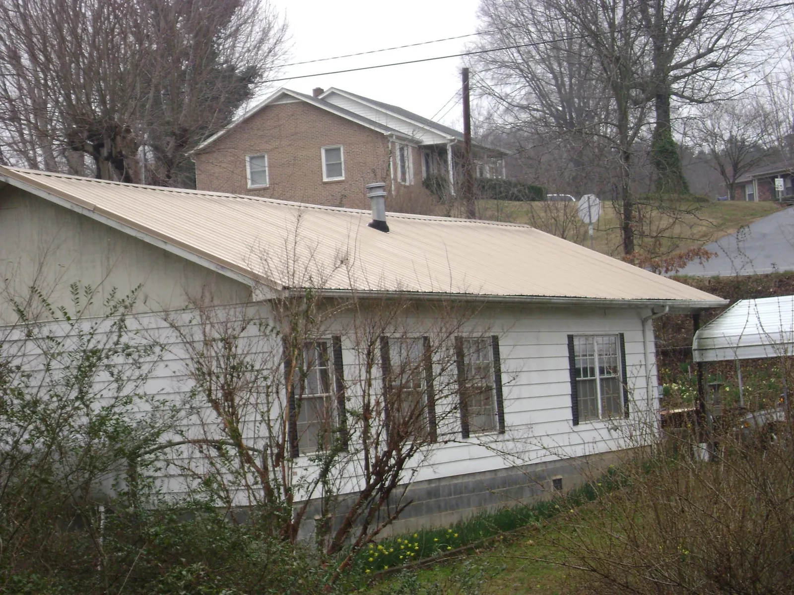 Tan metal roof on a white sided house set into a hillside — Commercial Roofing by Roofing Brothers in Somerville